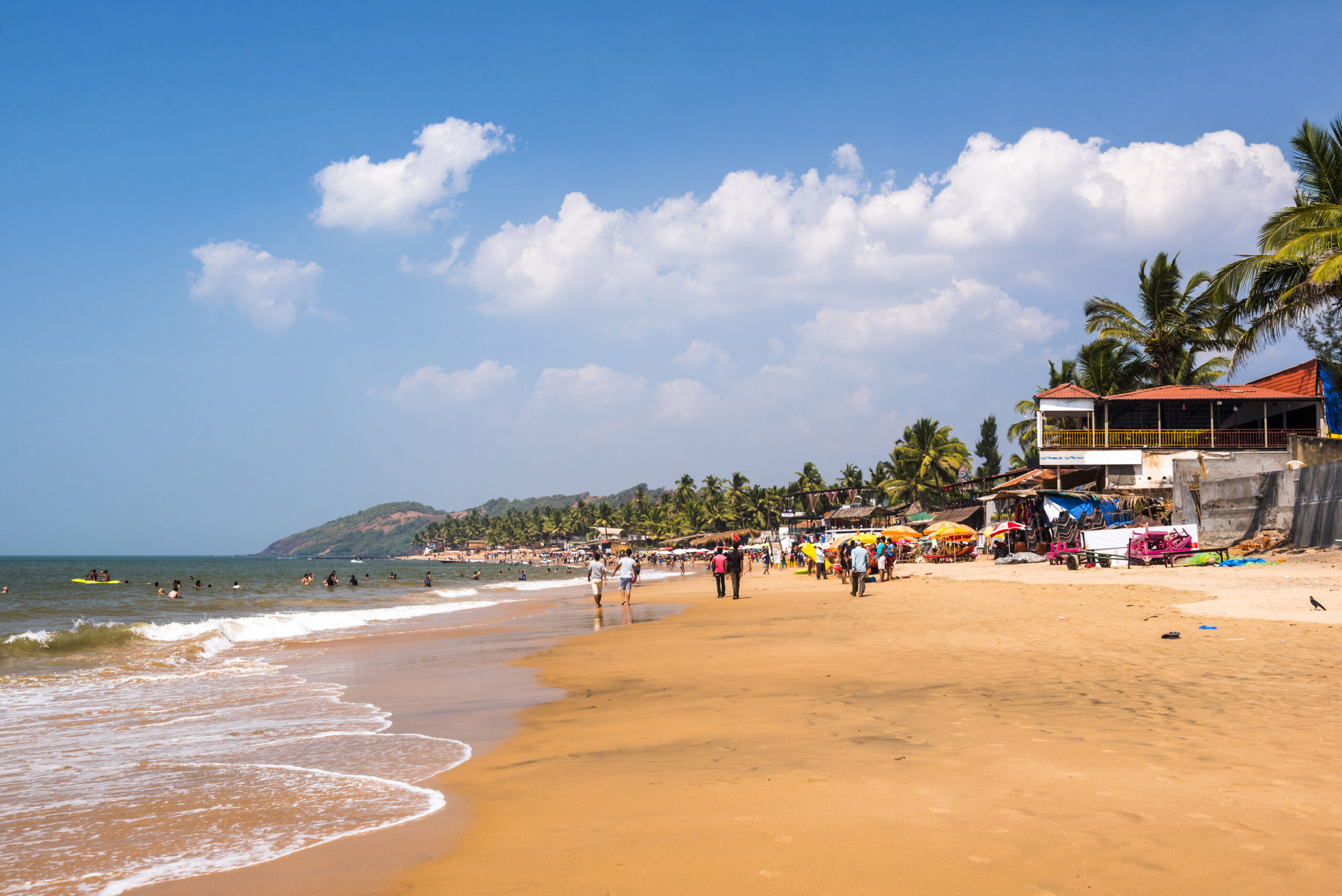 Tourists at tropical, sandy Anjuna Beach on the Goa coast with blue sky, India